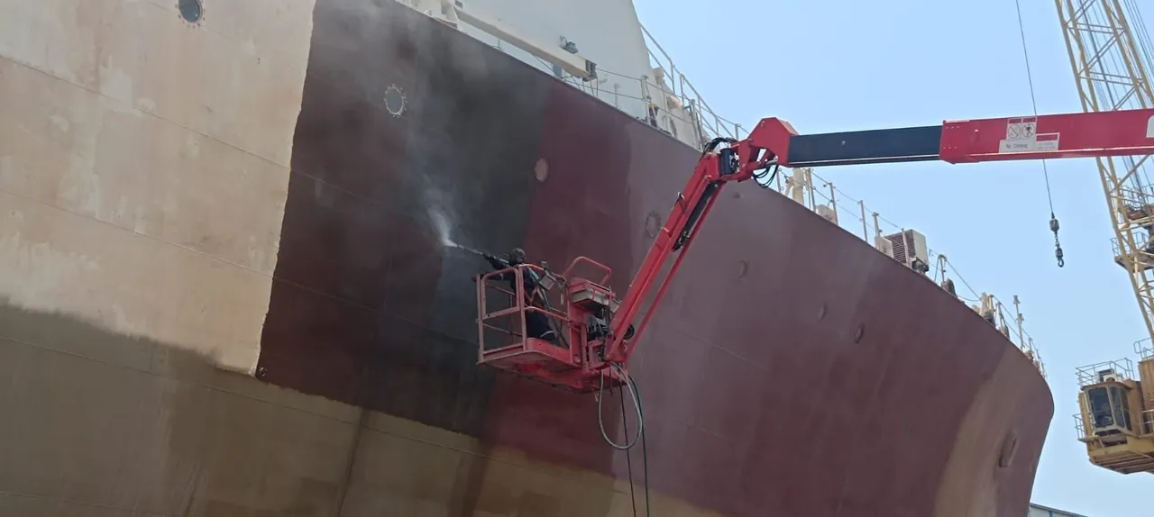 Hull surface preparation and coating from a boom lift, vessel in dry dock.